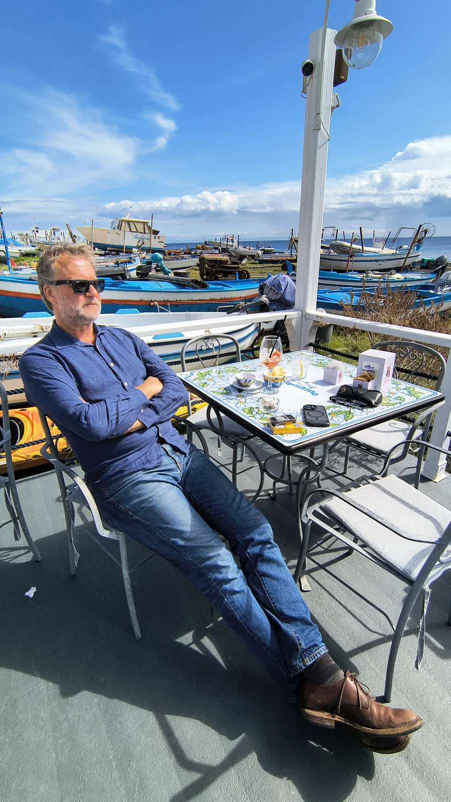 Robert Gerhards sitzt in einem Café an einem Hafen mit bunten Fischerbooten