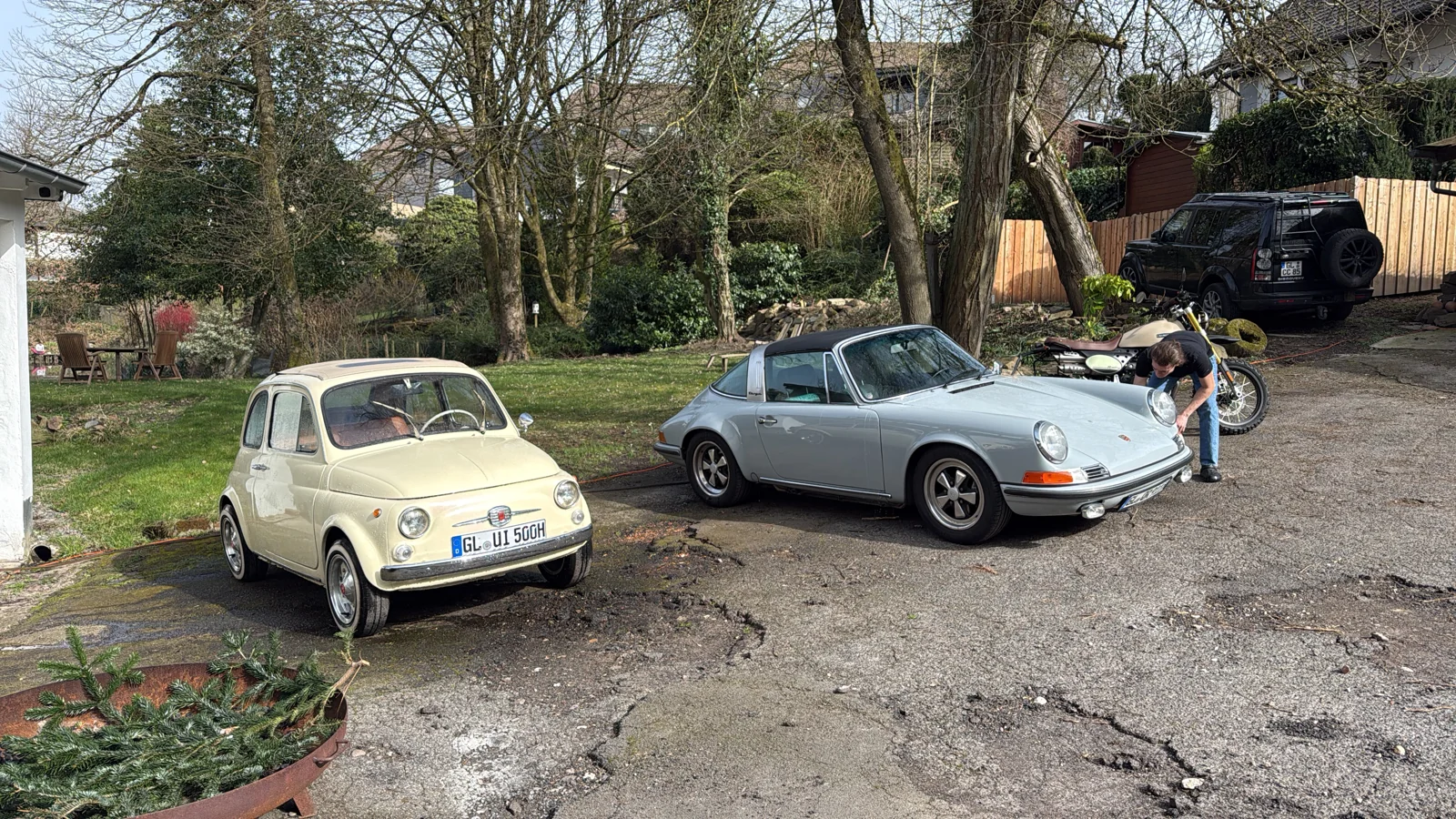 Klassischer Fiat 500 und silberner Porsche auf dem Hof