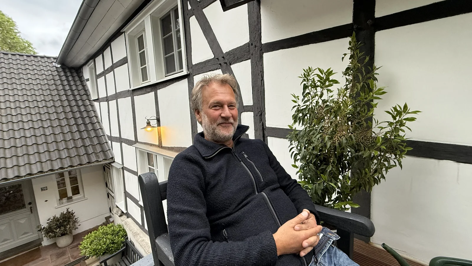 Robert Gerhards sitzt entspannt vor der Fachwerkfassade auf Gut Bechhausen